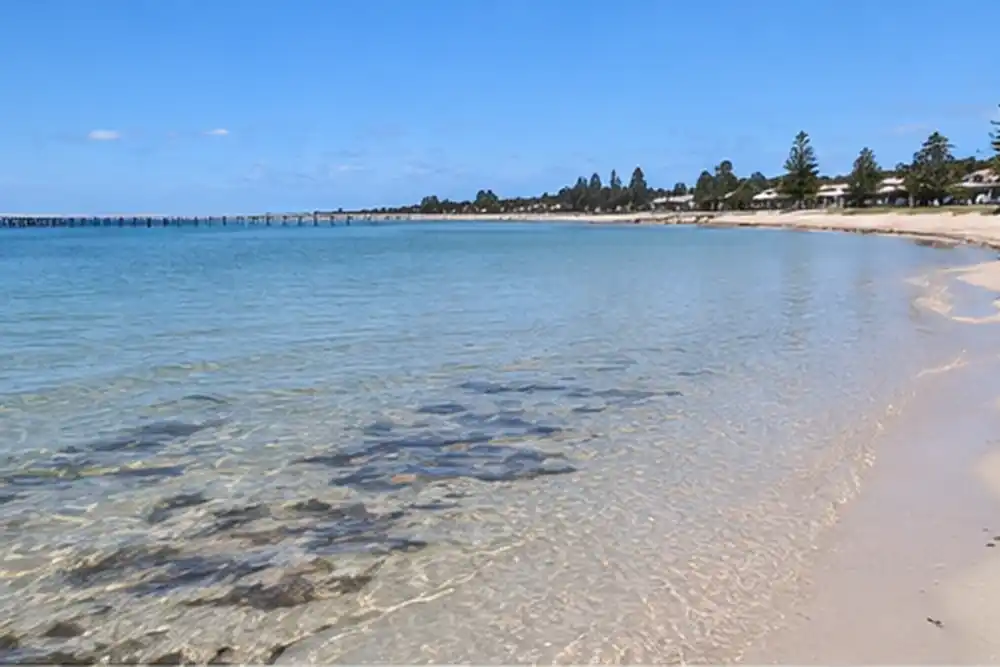 Calm sandy beach with clear shallow water and a distant jetty
